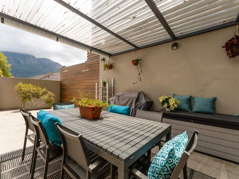 Covered outdoor patio area featuring tiled flooring, a timber-clad feature wall, and a corrugated roof structure, offering a functional space for outdoor dining.