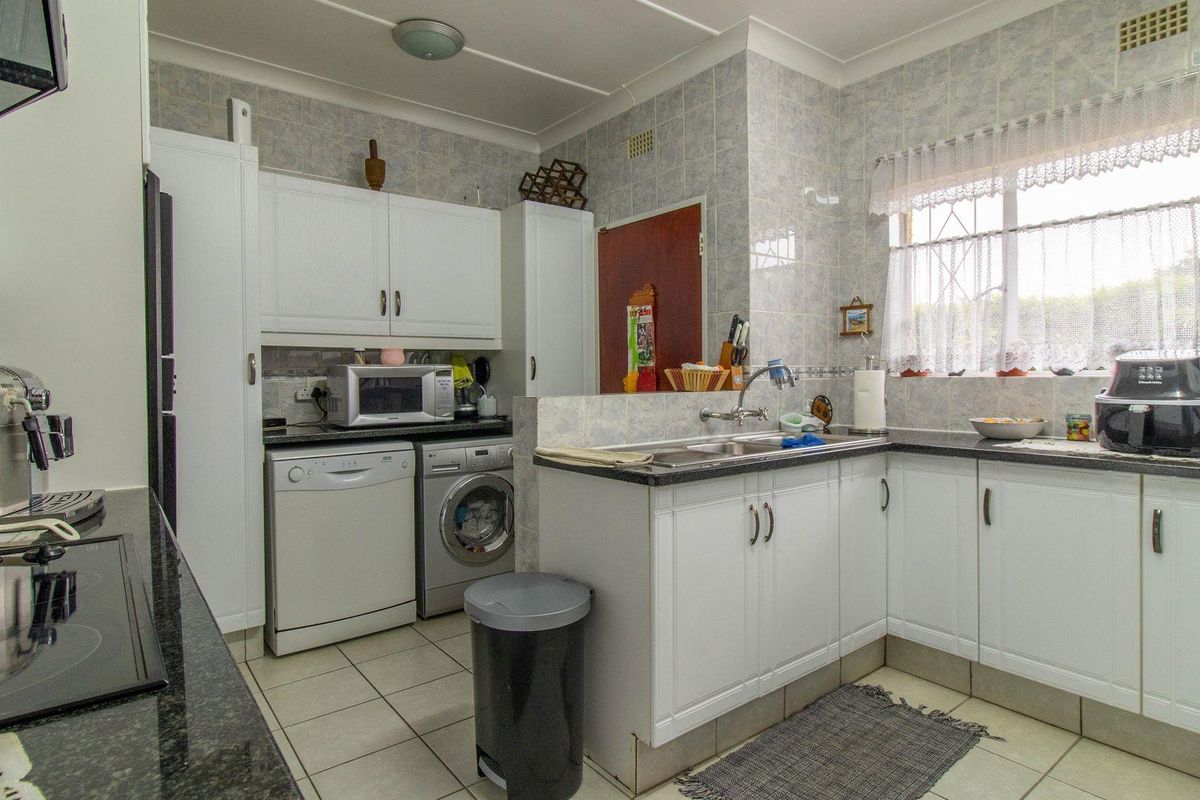 A functional kitchen featuring white cabinetry, dark granite countertops, tiled walls, and integrated space for laundry appliances.