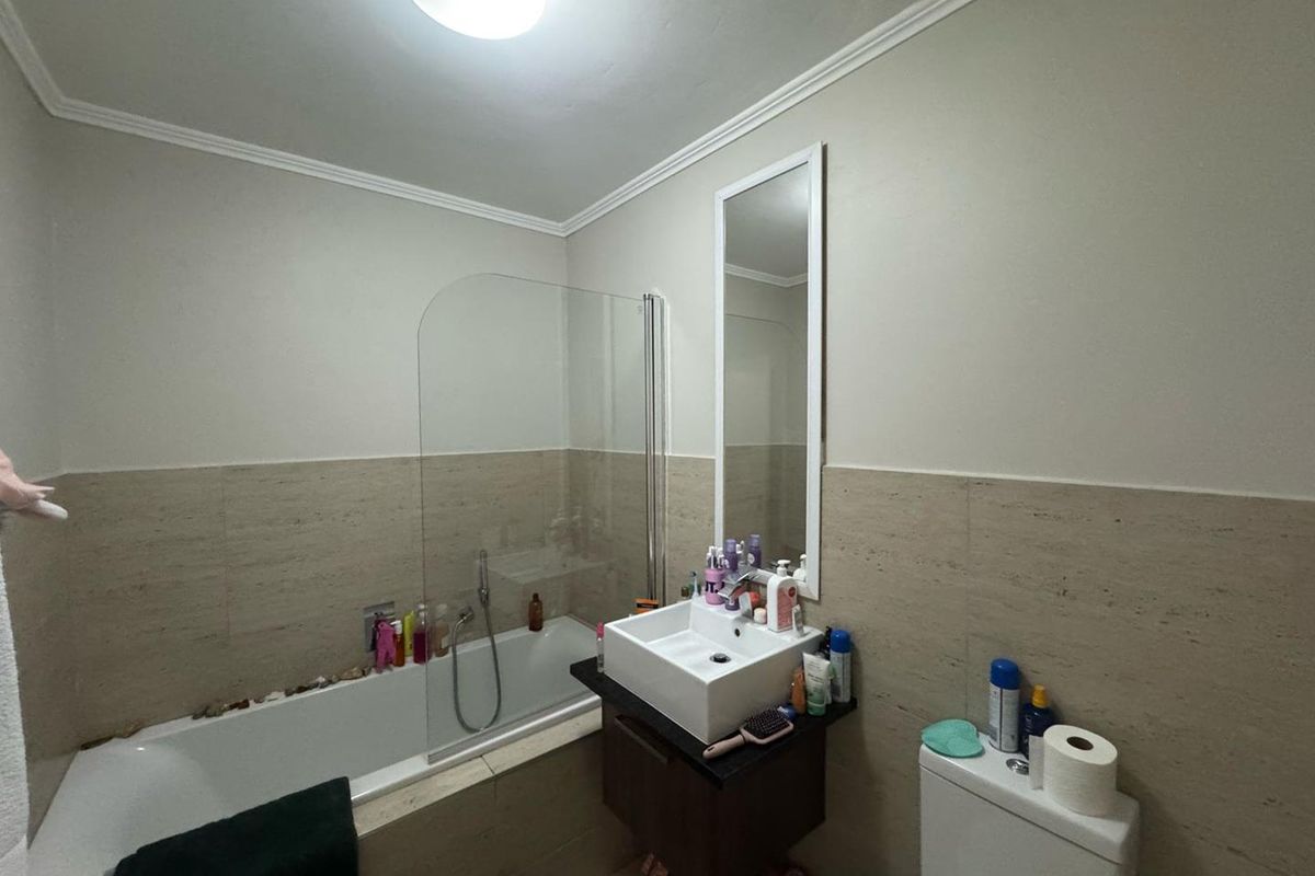 A functional bathroom featuring a bathtub with a glass screen, a wall-mounted vanity with a vessel sink, and a wall-mounted toilet.