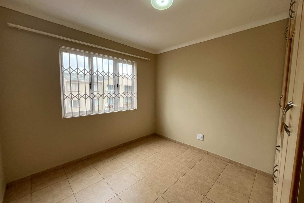 A clean, empty bedroom featuring neutral tiled flooring, a built-in wardrobe, and a window fitted with a security gate.