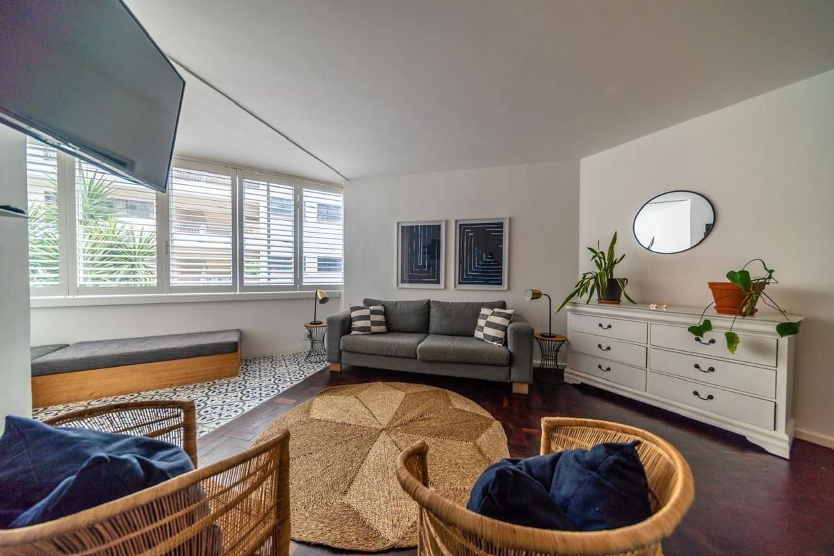 A bright living room featuring dark hardwood flooring, a decorative tiled window nook, and white plantation shutters.