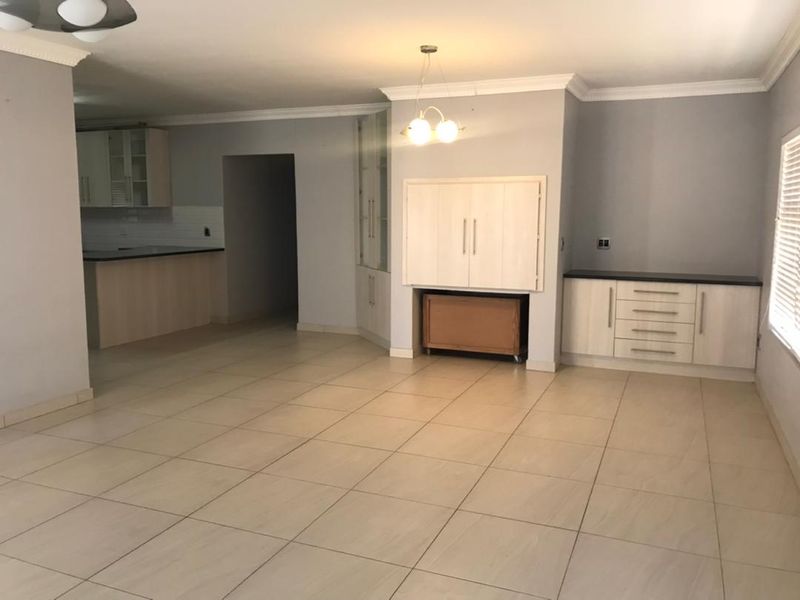 Spacious open-plan living and kitchen area featuring neutral tiled flooring, built-in cabinetry, and coved cornicing, offering a versatile layout for modern living.