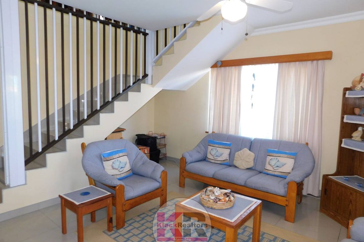 A living room area featuring a staircase with a metal balustrade, tiled flooring, and a ceiling fan.