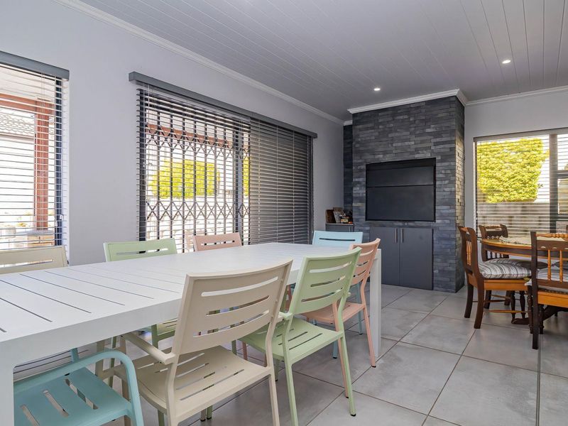 A bright dining area featuring tiled flooring, recessed lighting, and a prominent stone-clad built-in fireplace, with large windows fitted with venetian blinds.