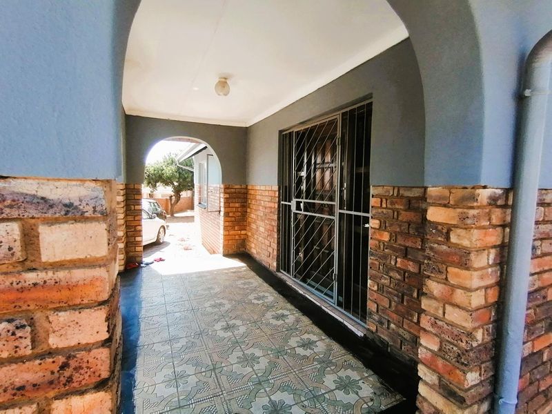 A covered patio area featuring brick pillars, arched architectural details, and patterned floor tiles, secured with a metal gate.