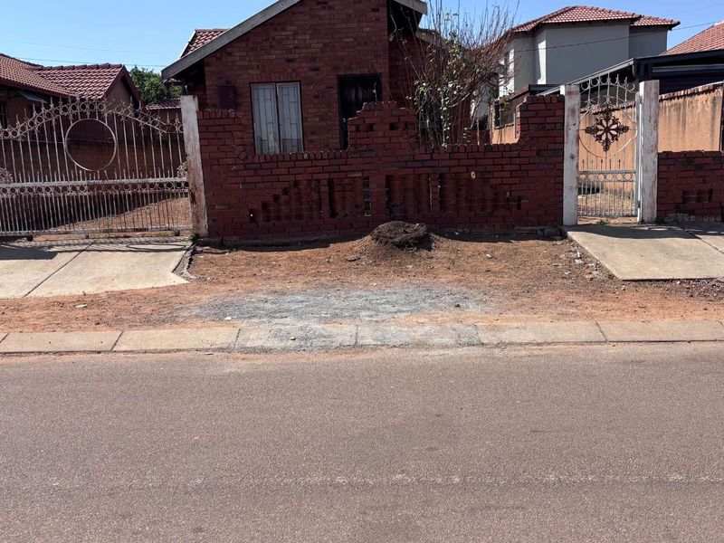 Front elevation of a brick house featuring a gated entrance, boundary wall, and concrete driveway access from the street.