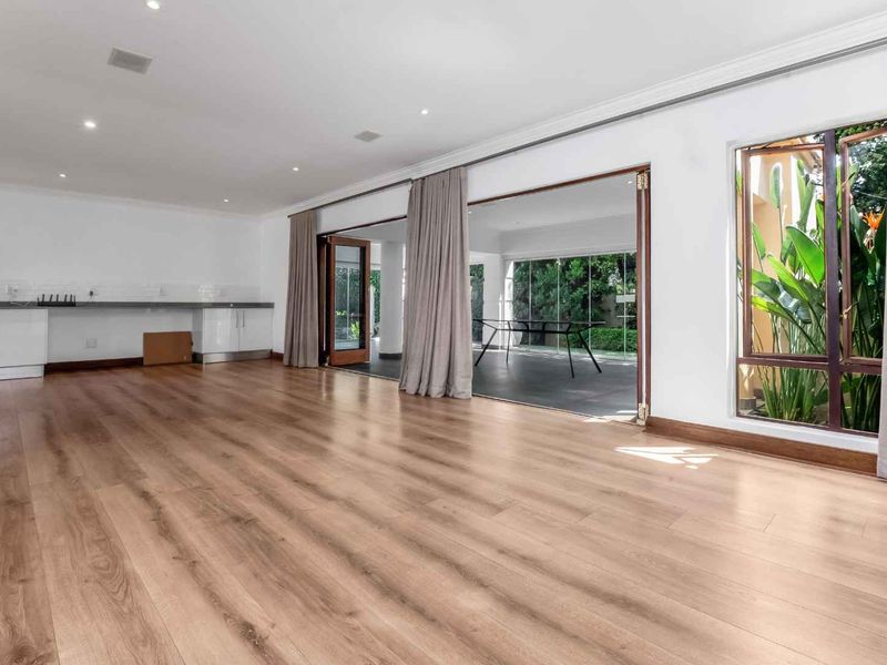 Spacious open-plan living area featuring light wood-look laminate flooring, built-in cabinetry with stone counters, and seamless access to the patio through bi-fold doors.