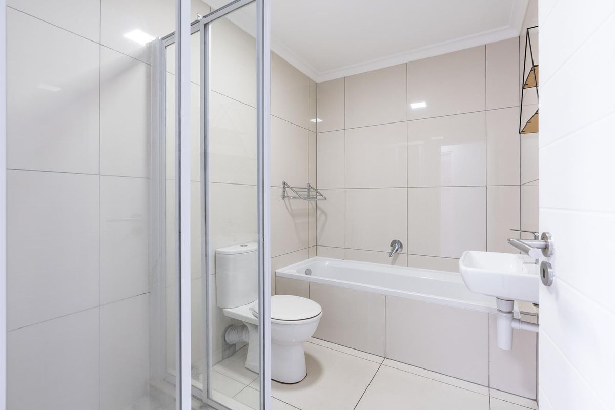 Modern bathroom featuring a built-in bathtub, glass shower enclosure, wall-mounted basin, and neutral floor-to-ceiling tiling.