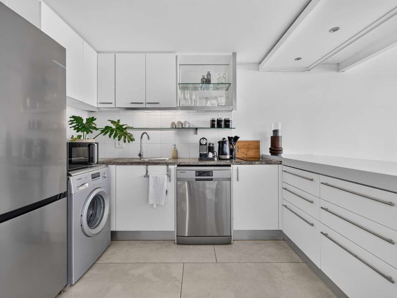 Modern kitchen featuring white cabinetry, stone countertops, integrated dishwasher, and built-in washing machine, offering a clean and functional workspace.