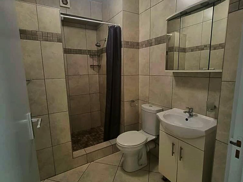 A functional bathroom featuring a tiled shower enclosure, a vanity unit with a basin, a mirrored medicine cabinet, and neutral floor-to-ceiling wall tiles.