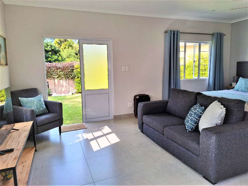 A bright bedroom featuring tiled flooring, a glass panel door providing garden access, and a window with natural light.