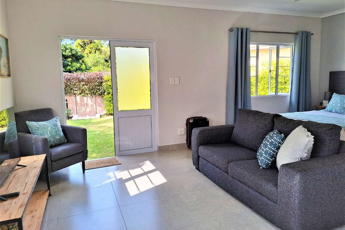 A bright bedroom featuring tiled flooring, a glass panel door providing garden access, and a window with natural light.