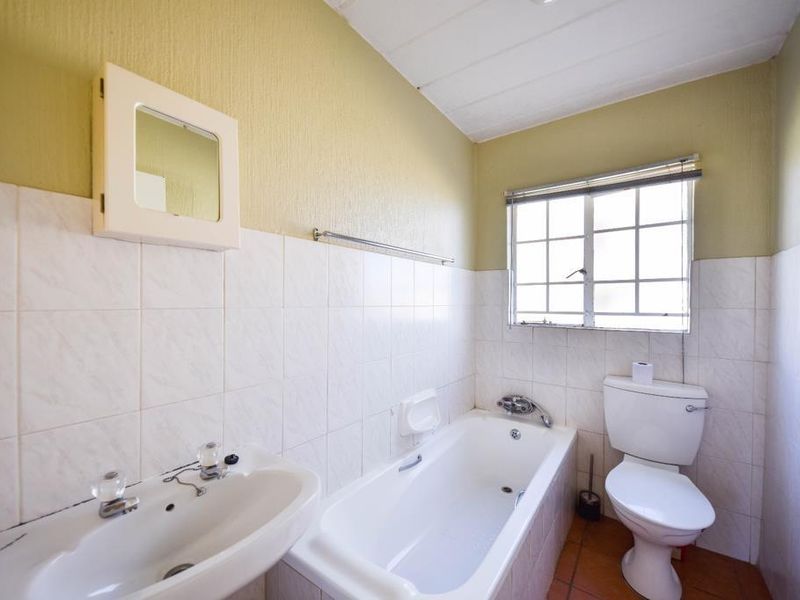 A dated bathroom featuring a standard bathtub, pedestal basin, and toilet with tiled walls and flooring, ready for a modern renovation.