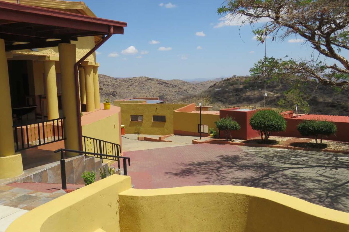 An elevated view of the rear exterior area featuring a covered patio, paved driveway, and surrounding landscape with mountain views.