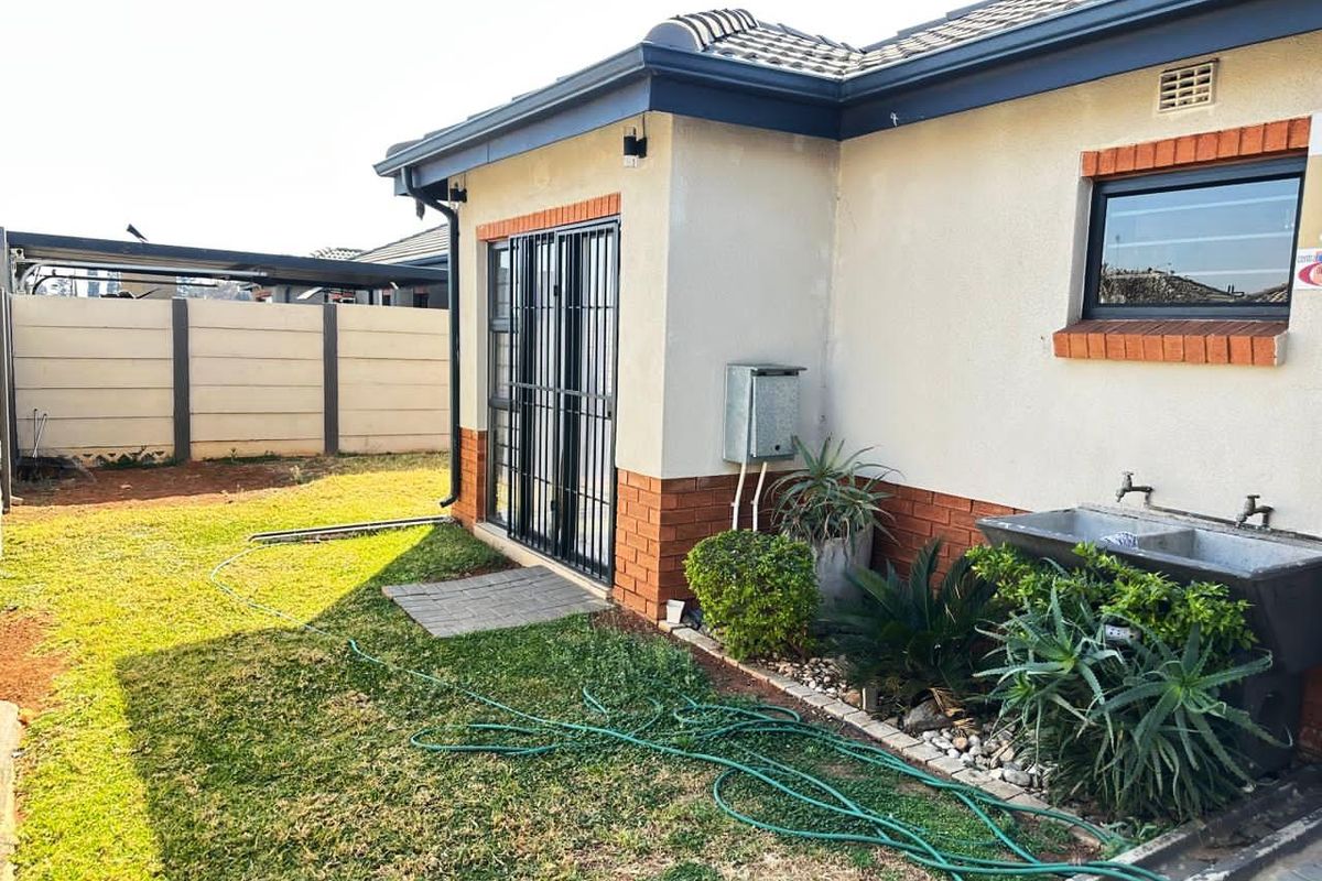 Rear exterior view of the house featuring a brick and plaster facade, sliding door with security gate, and a functional outdoor utility sink.