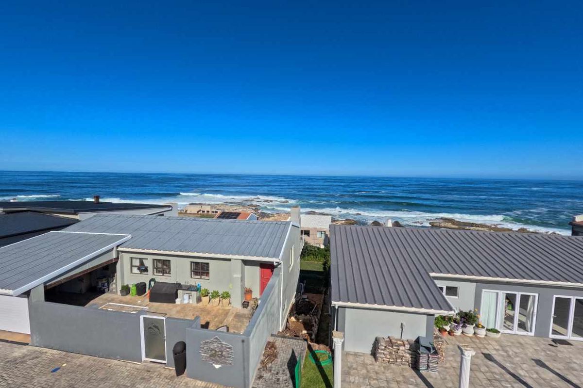 Aerial view of coastal residential properties featuring metal roofing, paved driveways, and direct ocean views.