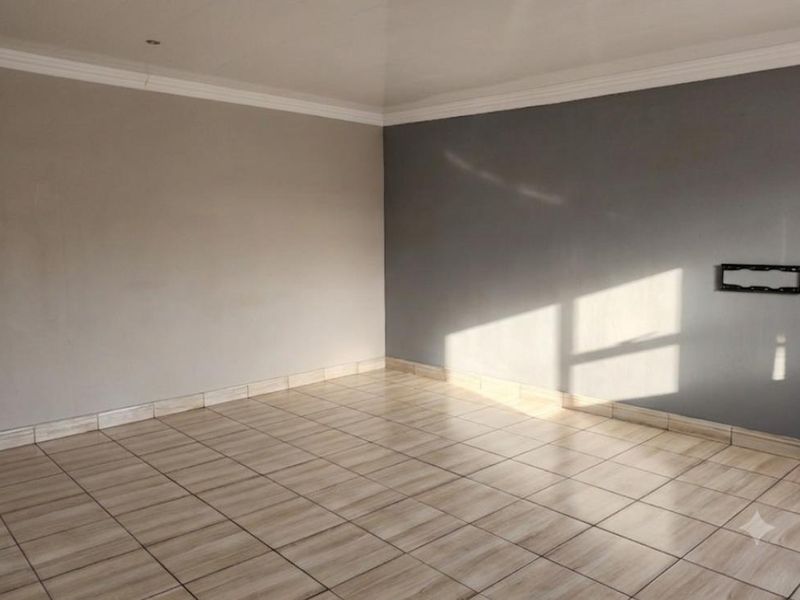 An empty living room featuring neutral-toned walls, tiled flooring, and a wall-mounted television bracket, offering a clean and versatile space.