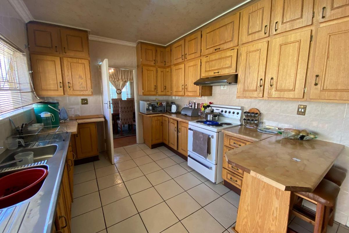 A functional kitchen featuring extensive wooden cabinetry, tiled flooring, a breakfast counter, and a tiled backsplash, offering a traditional layout with ample storage space.