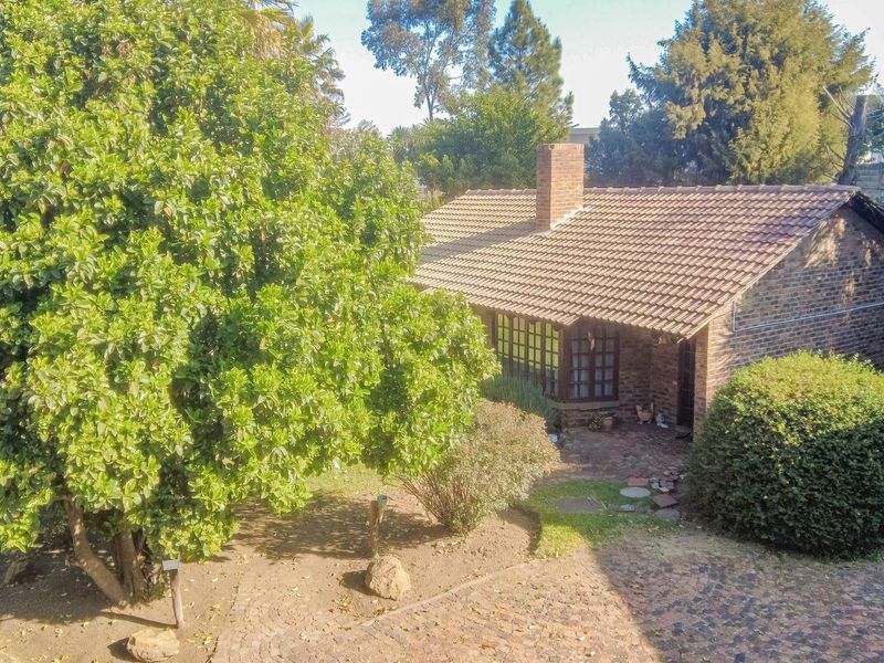 Rear view of a brick townhouse featuring a tiled roof, chimney, and a paved patio area surrounded by mature garden landscaping.