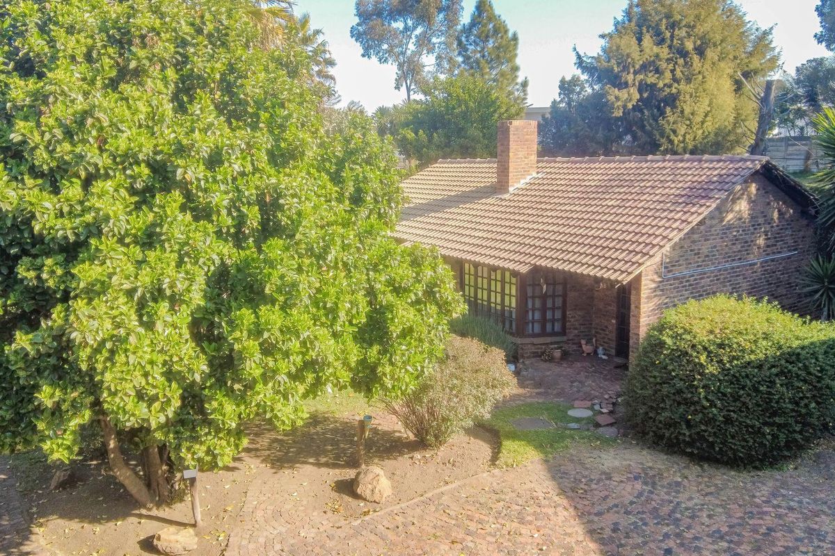Rear view of a brick townhouse featuring a tiled roof, chimney, and a paved patio area surrounded by mature garden landscaping.