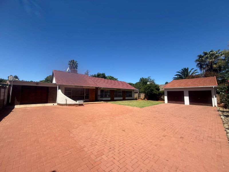 Front view of a residential property featuring a large paved driveway, a main house with a tiled roof, and a separate double garage structure.