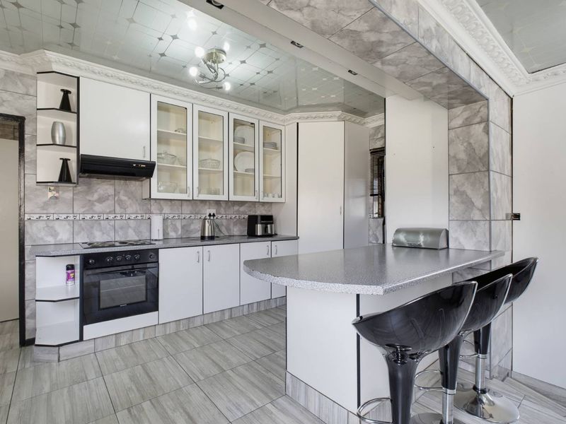 A functional kitchen featuring white cabinetry, laminate countertops, a breakfast bar, built-in oven, hob, and decorative ceiling panels with integrated lighting.