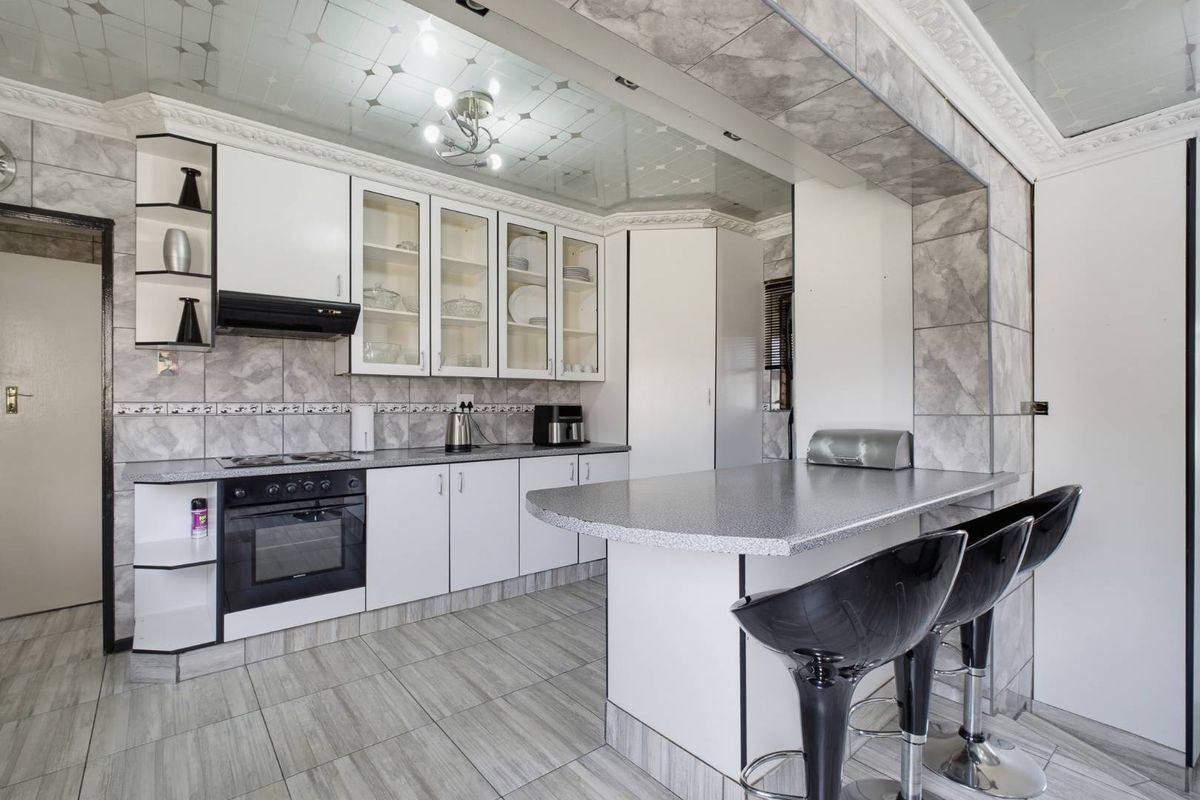 A functional kitchen featuring white cabinetry, laminate countertops, a breakfast bar, built-in oven, hob, and decorative ceiling panels with integrated lighting.