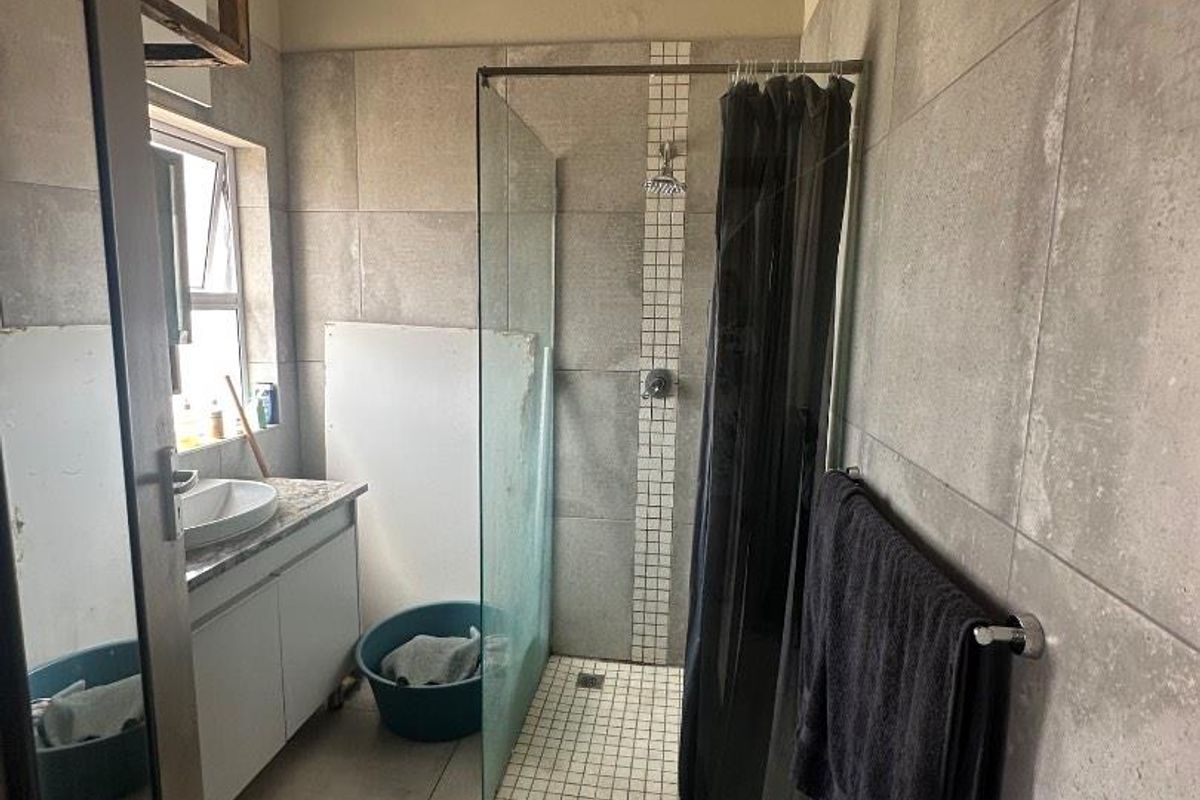 A functional bathroom featuring a glass-enclosed shower with mosaic tile accents, a vanity with a basin, and large-format grey wall tiles.