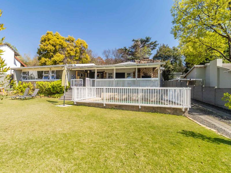 Rear view of the property featuring a swimming pool, covered patio area, and a well-maintained garden with stone architectural details.