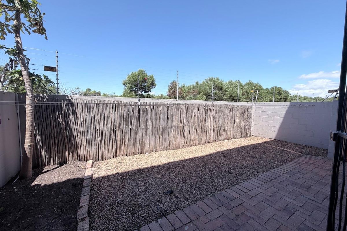 A private rear courtyard featuring paved flooring, a gravel area, and perimeter boundary walls with security fencing.