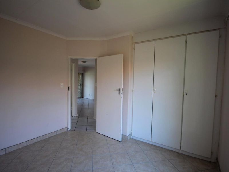 An empty bedroom featuring built-in cupboards, tiled flooring, and neutral wall finishes, offering a blank canvas for personalization.
