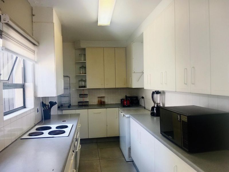 A functional galley-style kitchen featuring ample built-in cabinetry, laminate countertops, a tiled backsplash, and an integrated electric hob.