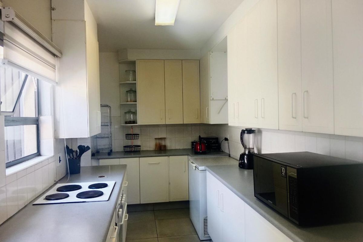 A functional galley-style kitchen featuring ample built-in cabinetry, laminate countertops, a tiled backsplash, and an integrated electric hob.