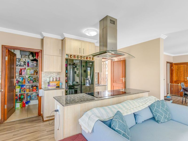 Open-plan kitchen featuring light wood cabinetry, a central island with an electric hob and extractor fan, and an adjacent walk-in pantry.