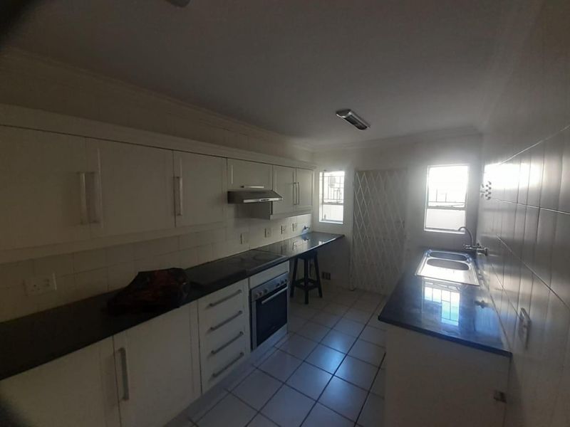 A functional kitchen featuring white cabinetry, dark granite countertops, a built-in oven with extractor fan, and tiled flooring.