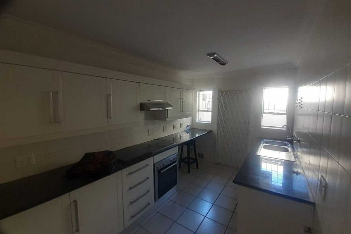 A functional kitchen featuring white cabinetry, dark granite countertops, a built-in oven with extractor fan, and tiled flooring.