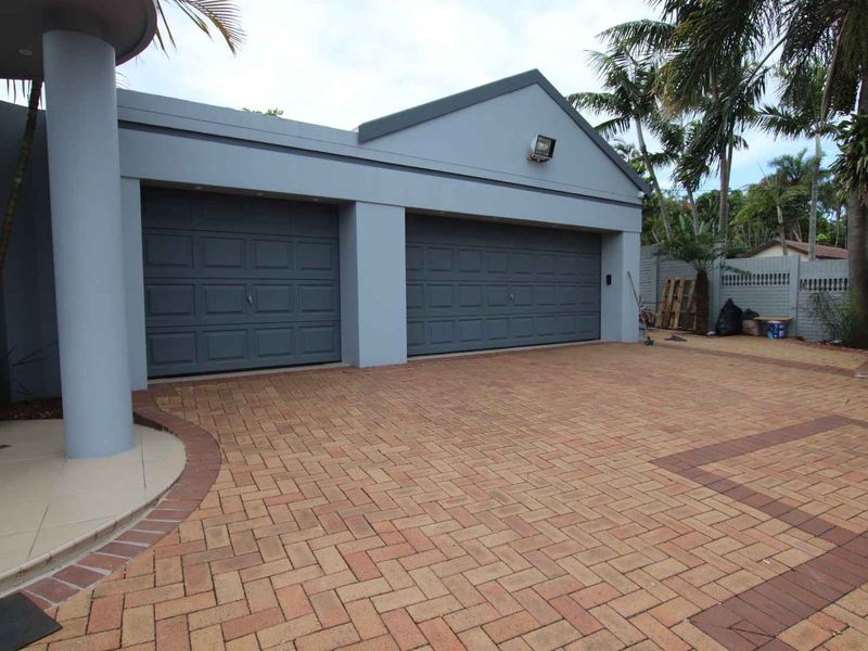 A well-maintained front exterior view featuring a double garage with paved driveway and a covered entrance area.