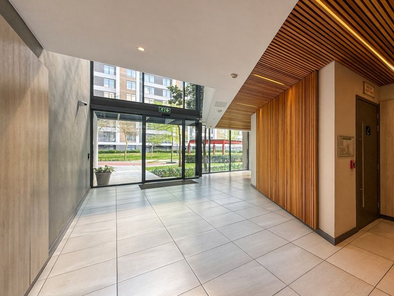 Modern entrance lobby featuring high ceilings with timber slat detailing, large glass windows, and clean tiled flooring, providing a bright and welcoming arrival space.