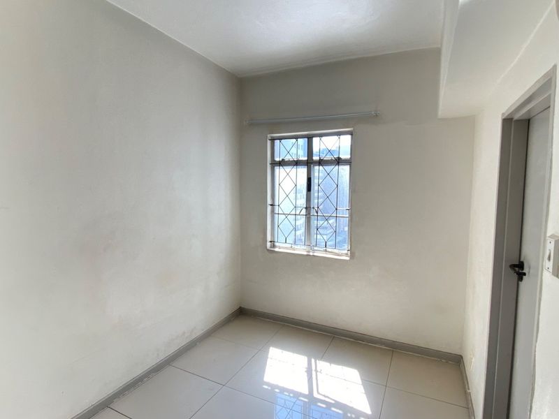 An empty bedroom featuring tiled flooring and a window with security bars, requiring minor cosmetic updates to the wall finishes.