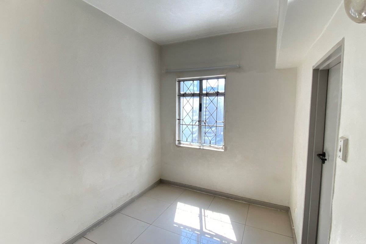 An empty bedroom featuring tiled flooring and a window with security bars, requiring minor cosmetic updates to the wall finishes.