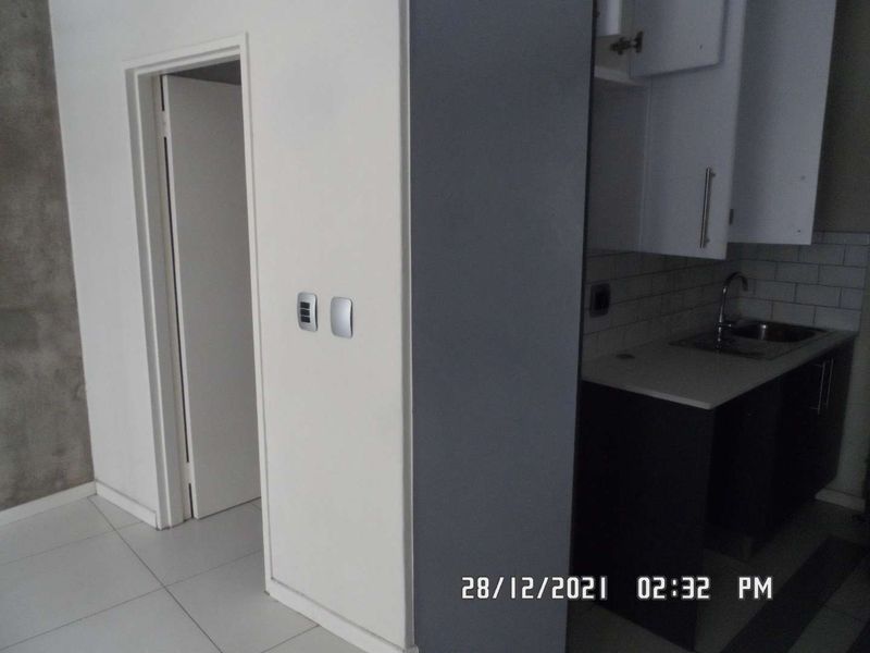 A compact kitchen area featuring built-in cabinetry, a sink, and a tiled backsplash, adjacent to a hallway entrance.