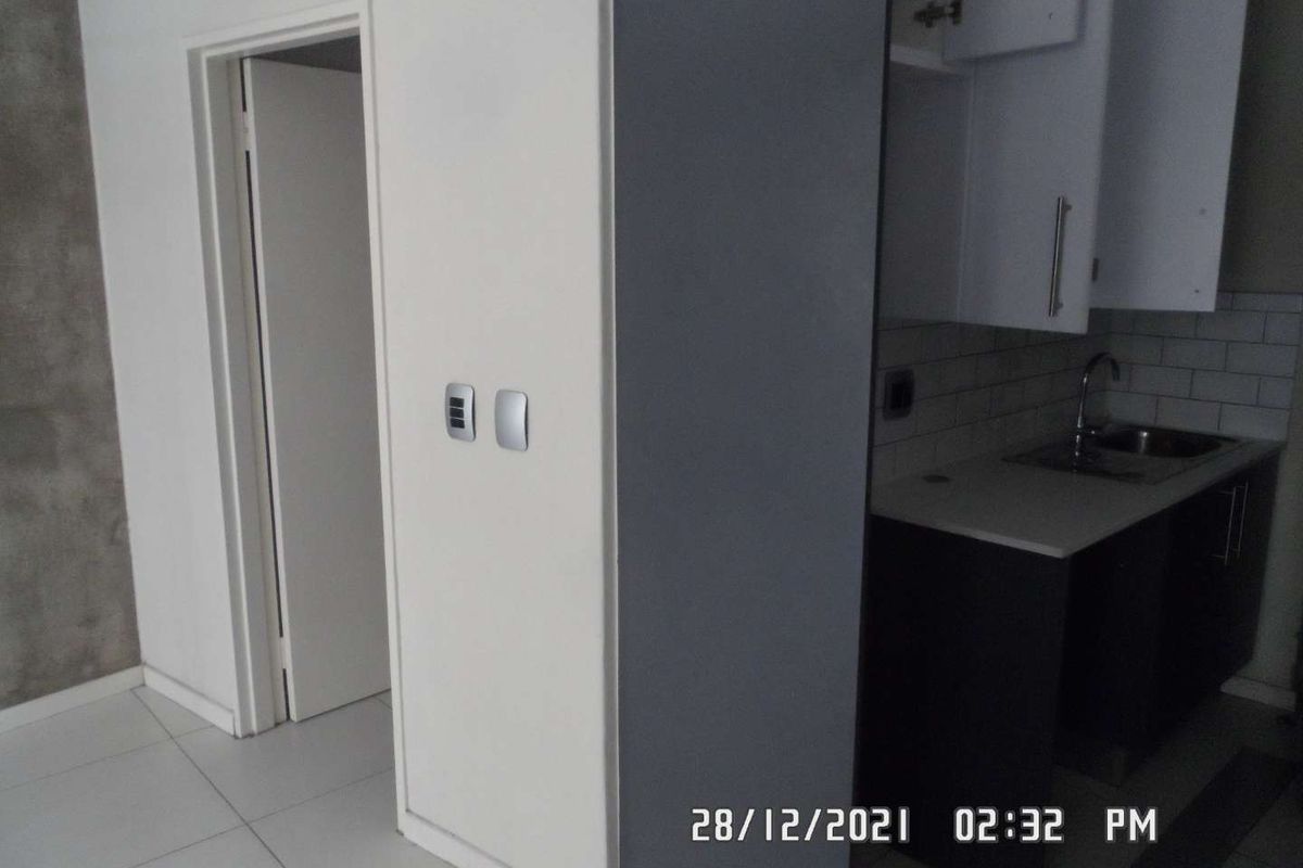 A compact kitchen area featuring built-in cabinetry, a sink, and a tiled backsplash, adjacent to a hallway entrance.
