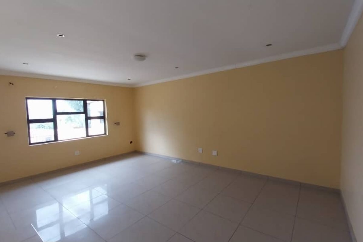 A spacious, empty living room featuring neutral wall tones, large windows for natural light, and polished floor tiles throughout.