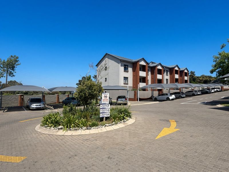 Exterior view of an apartment complex featuring paved parking areas with shade cloth carports and a landscaped central island.