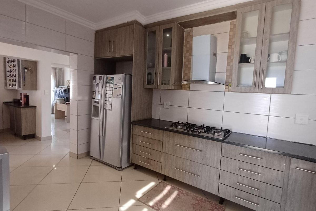 Modern kitchen featuring wood-finish cabinetry, granite countertops, a gas hob with extractor fan, and neutral tiled flooring throughout.