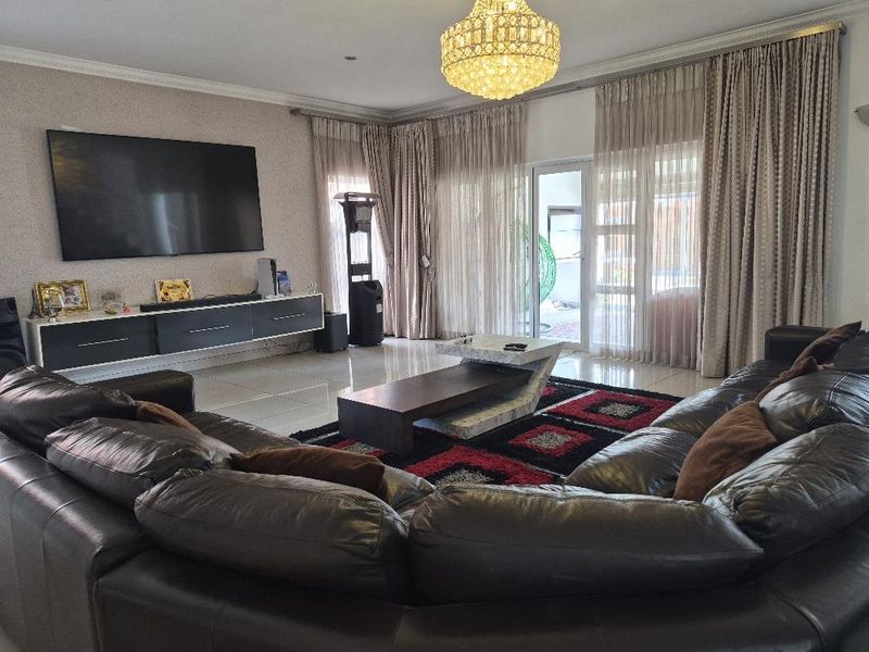 Spacious living room featuring large-format porcelain floor tiles, elegant crystal chandelier lighting, and direct access to the patio through sliding glass doors.