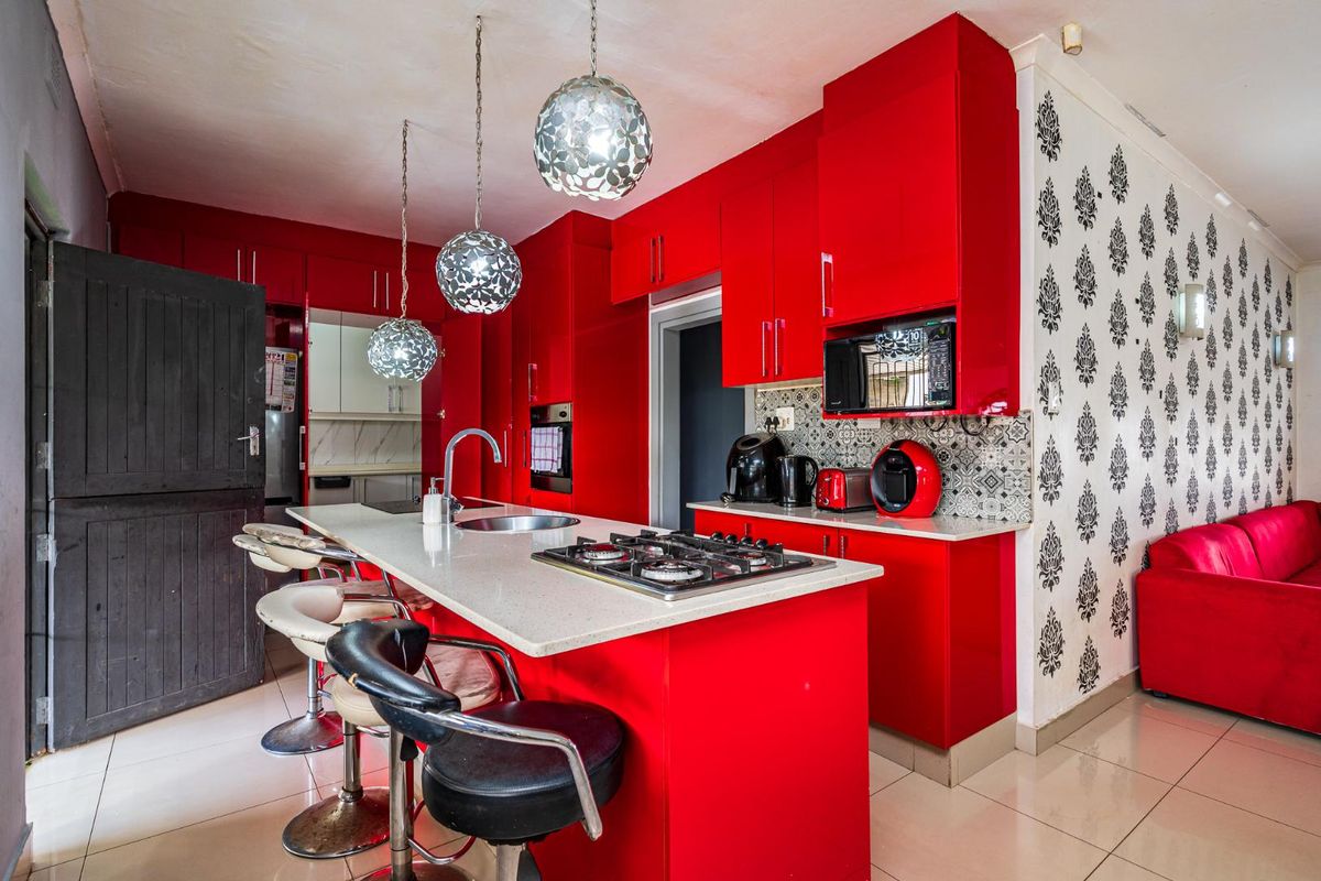 Modern kitchen featuring vibrant red cabinetry, a central island with a built-in gas hob, stone countertops, and decorative patterned wall tiling.