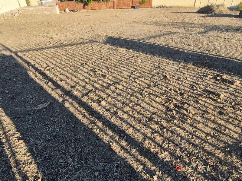 A large, undeveloped outdoor garden area featuring perimeter walling and metal fencing, currently requiring landscaping and ground maintenance.