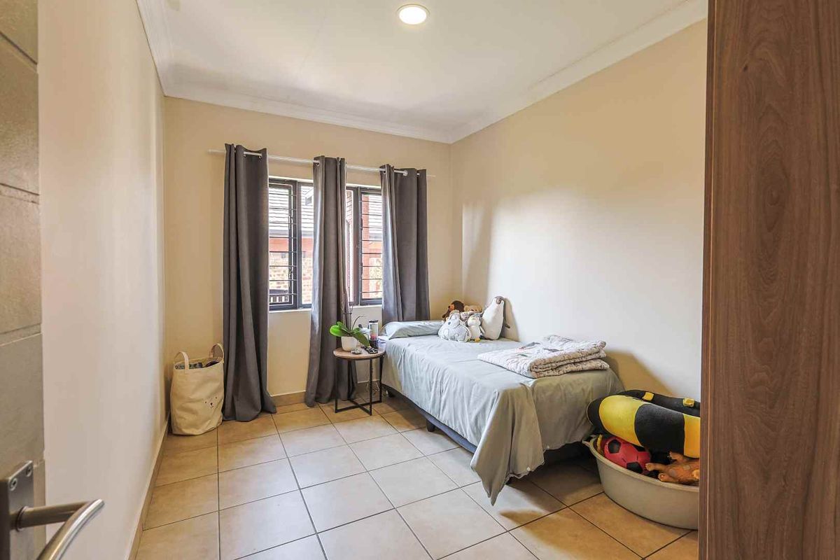 A functional bedroom featuring tiled flooring, neutral wall finishes, and dual windows with security bars, providing natural light and a practical living space.