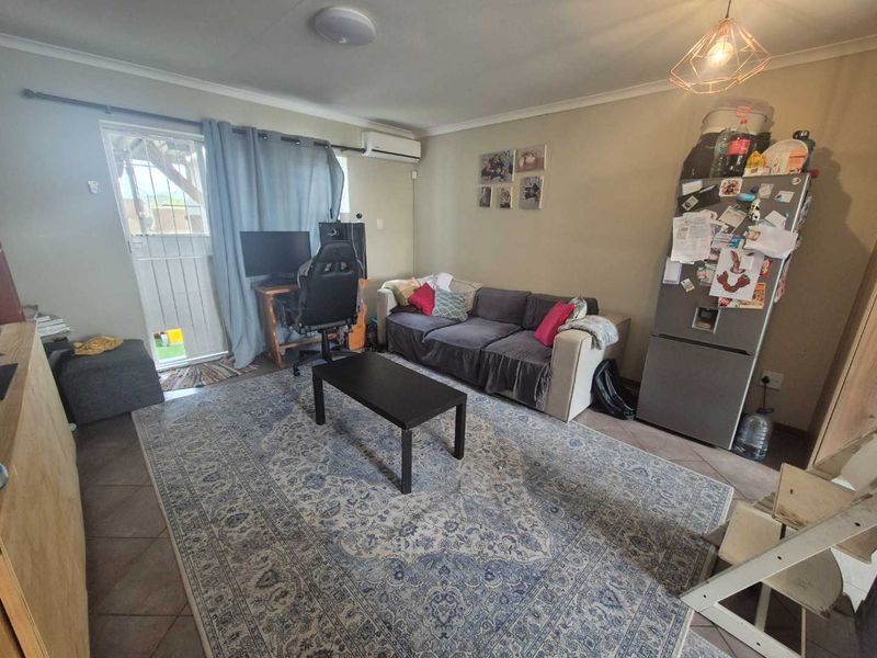 A functional living room featuring tiled flooring, a split-system air conditioner, and direct access to an outdoor area via a security gate.